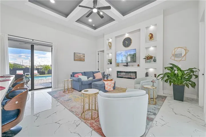 Living room featuring coffered ceiling, a towering ceiling, a ceiling fan, marble finish floor, and a glass covered fireplace