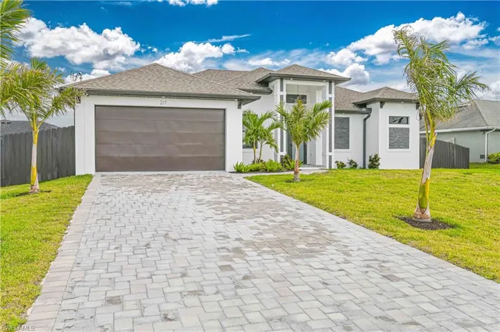 Prairie-style house featuring an attached garage, fence, decorative driveway, a front yard, and stucco siding