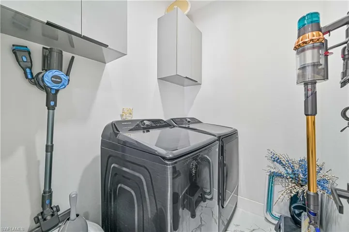 Clothes washing area featuring marble finish floor, separate washer and dryer, cabinet space, and baseboards