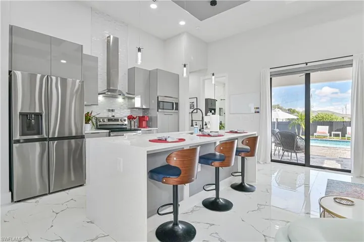 Kitchen featuring wall chimney exhaust hood, modern cabinets, marble finish floor, stainless steel appliances, and gray cabinetry