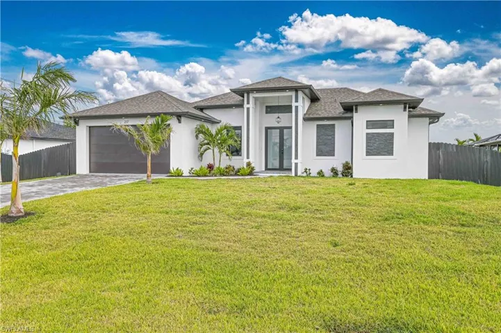 Prairie-style house with an attached garage, fence, decorative driveway, french doors, and a front lawn