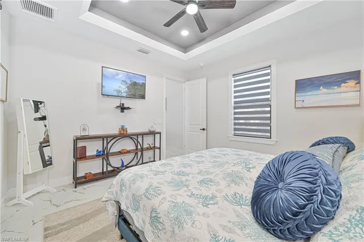 Bedroom featuring a tray ceiling, marble finish floor, visible vents, a ceiling fan, and baseboards