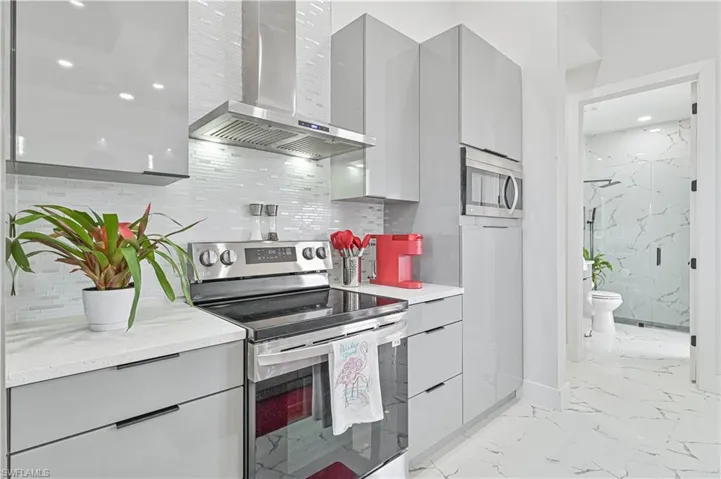 Kitchen featuring wall chimney exhaust hood, gray cabinets, stainless steel appliances, and modern cabinets