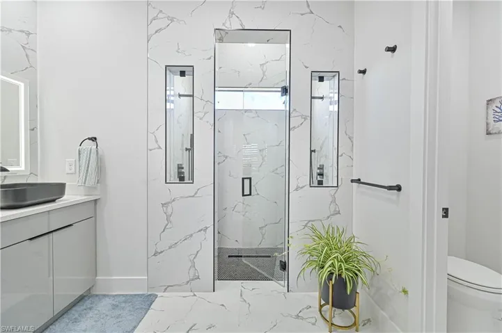 Full bath with marble finish floor, toilet, vanity, and a marble finish shower