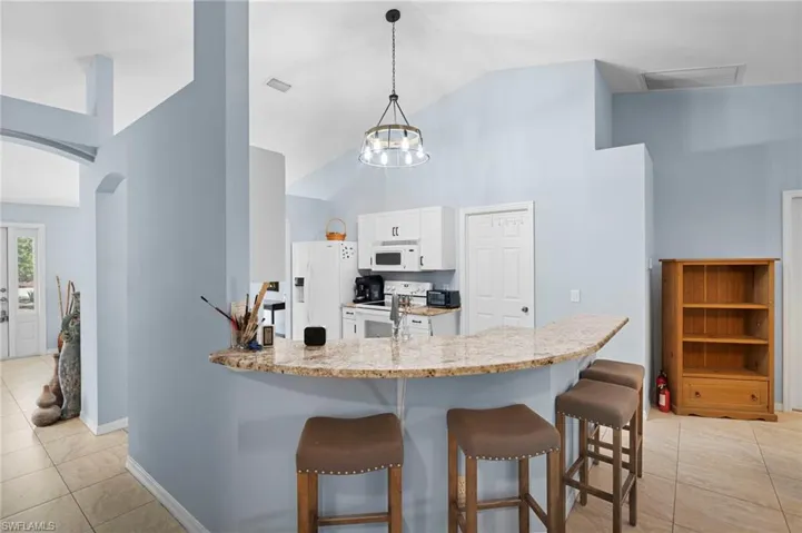 Kitchen with light tile patterned flooring, arched walkways, a breakfast bar area, white cabinetry, and a peninsula