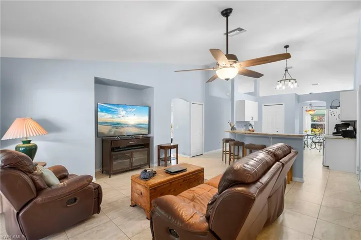 Living room featuring arched walkways, a ceiling fan, vaulted ceiling, hanging lights, and light tile patterned floors