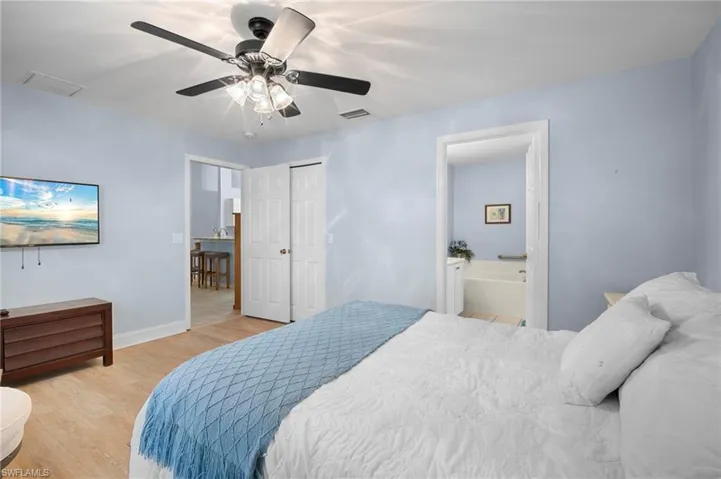 Bedroom featuring light wood-style floors, ceiling fan, ensuite bath, and a closet