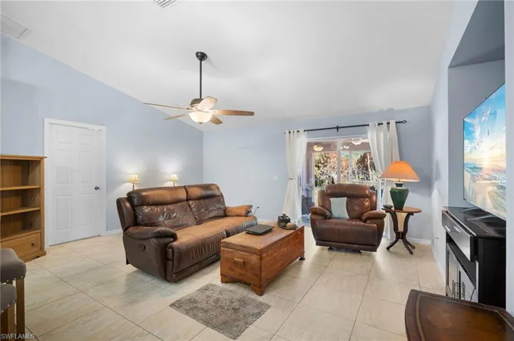 Living area featuring lofted ceiling, light tile patterned floors, and ceiling fan