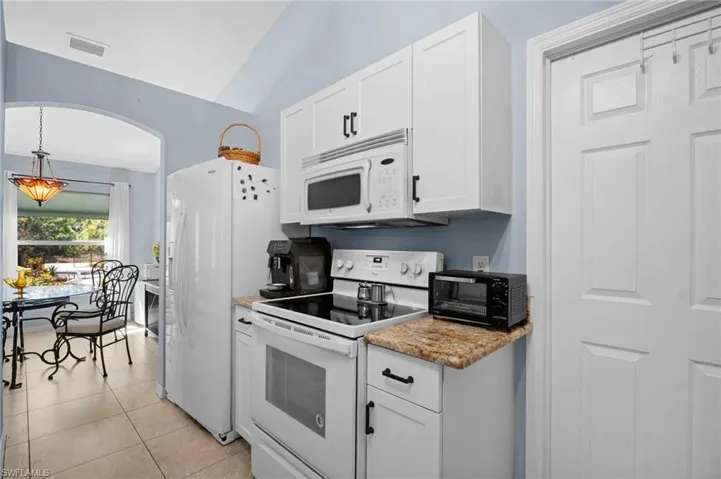 Kitchen with white appliances, white cabinetry, vaulted ceiling, light tile patterned floors, and arched walkways