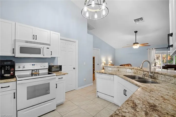 Kitchen featuring white appliances, white cabinets, light stone countertops, ceiling fan, and vaulted ceiling