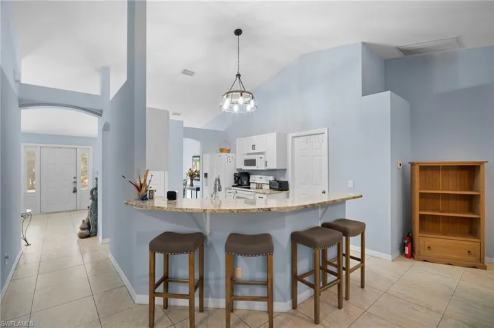 Kitchen with a kitchen breakfast bar, light stone countertops, white cabinetry, a peninsula, and a chandelier