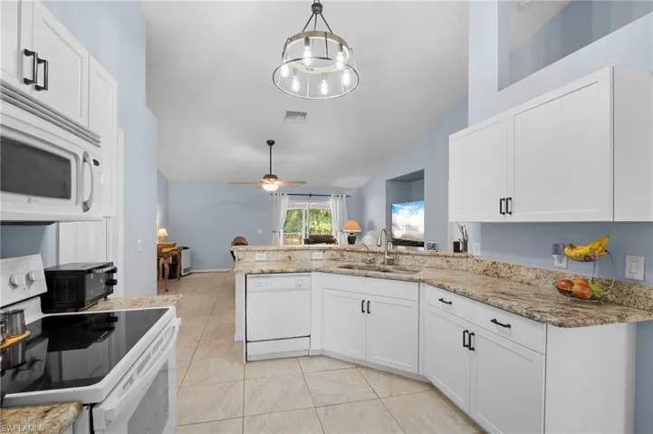 Kitchen with white appliances, white cabinets, a peninsula, and lofted ceiling