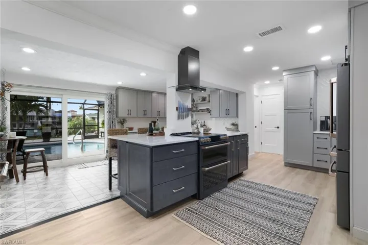 Kitchen featuring wall chimney range hood, appliances with stainless steel finishes, gray cabinetry, and light wood-type flooring