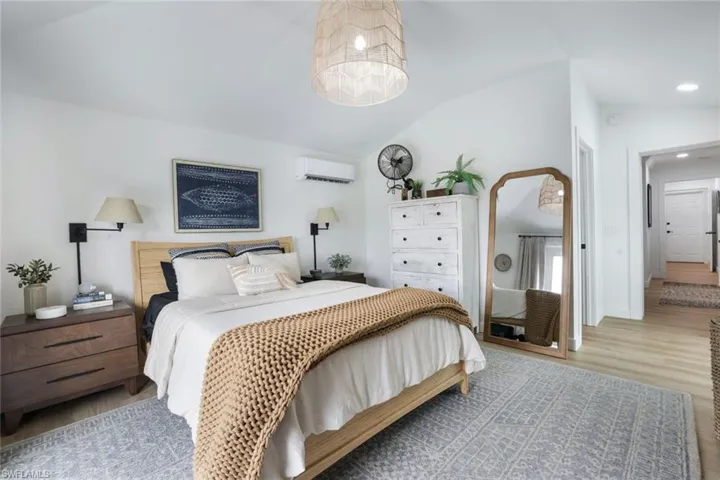 Bedroom with a wall mounted AC, vaulted ceiling, and light hardwood / wood-style flooring