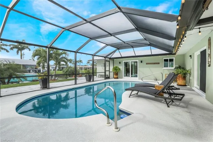 View of swimming pool featuring glass enclosure, a patio area, and a water view
