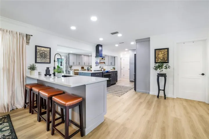 Kitchen with light hardwood / wood-style floors, crown molding, a breakfast bar, kitchen peninsula, and wall chimney range hood