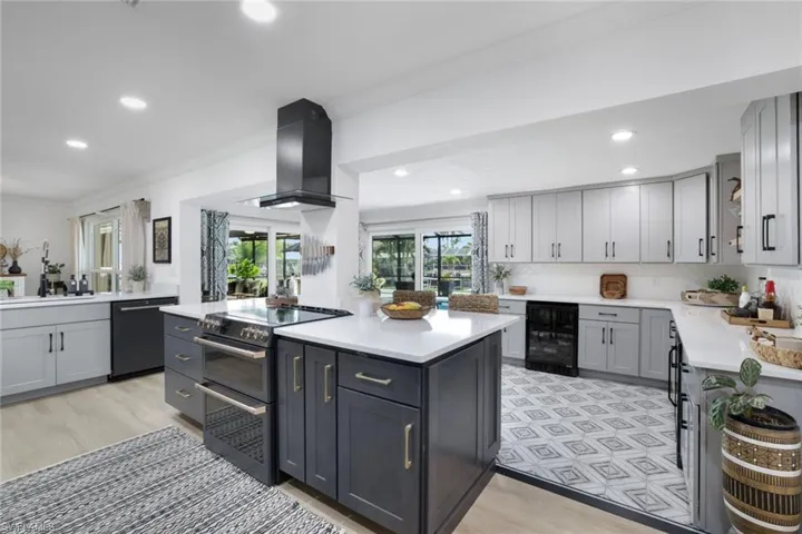 Kitchen with light hardwood / wood-style flooring, wine cooler, appliances with stainless steel finishes, gray cabinetry, and wall chimney range hood