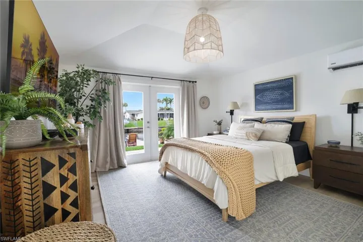 Bedroom with french doors, light wood-type flooring, vaulted ceiling, access to exterior, and an AC wall unit