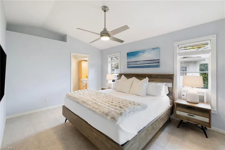 Bedroom with lofted ceiling, a ceiling fan, light tile patterned flooring, connected bathroom, and baseboards