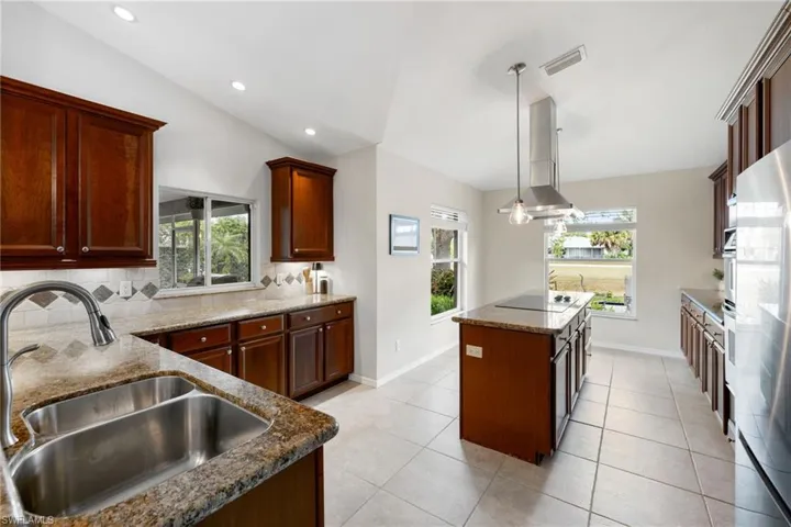 Kitchen featuring black electric cooktop, a sink, backsplash, a center island, and decorative light fixtures