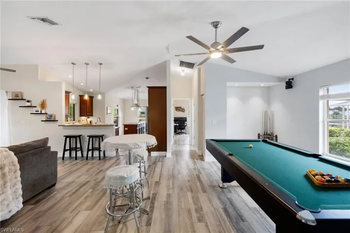Recreation room with ceiling fan, visible vents, vaulted ceiling, and wood finished floors