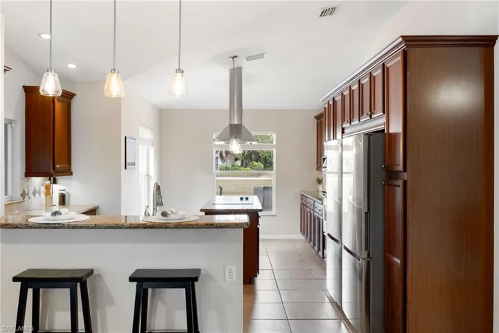 Kitchen with hanging light fixtures, a breakfast bar, freestanding refrigerator, and island range hood