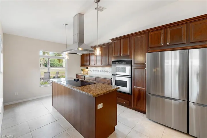 Kitchen featuring dark stone counters, a kitchen island, island exhaust hood, stainless steel appliances, and pendant lighting