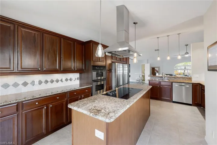 Kitchen with island exhaust hood, a kitchen island, appliances with stainless steel finishes, and decorative light fixtures