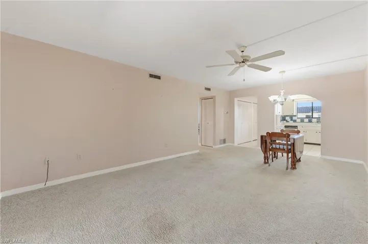 Empty room with hanging lights, ceiling fan, light carpet, and arched walkways