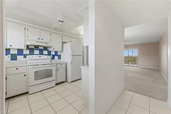 Kitchen with light colored carpet, white appliances, light countertops, white cabinetry, and a ceiling fan