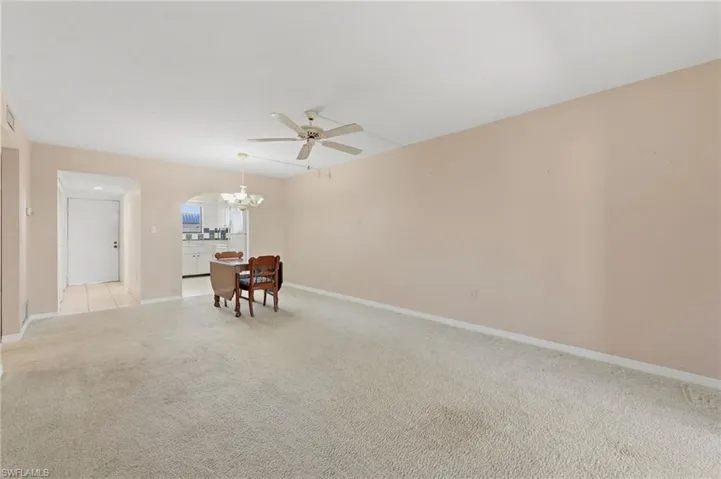 Empty room featuring a ceiling fan, light carpet, a chandelier, and arched walkways