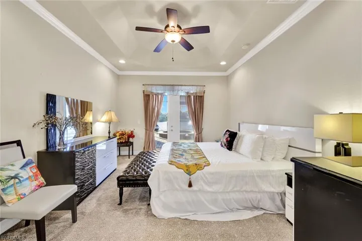 Bedroom featuring light carpet, french doors, access to outside, a tray ceiling, and ceiling fan