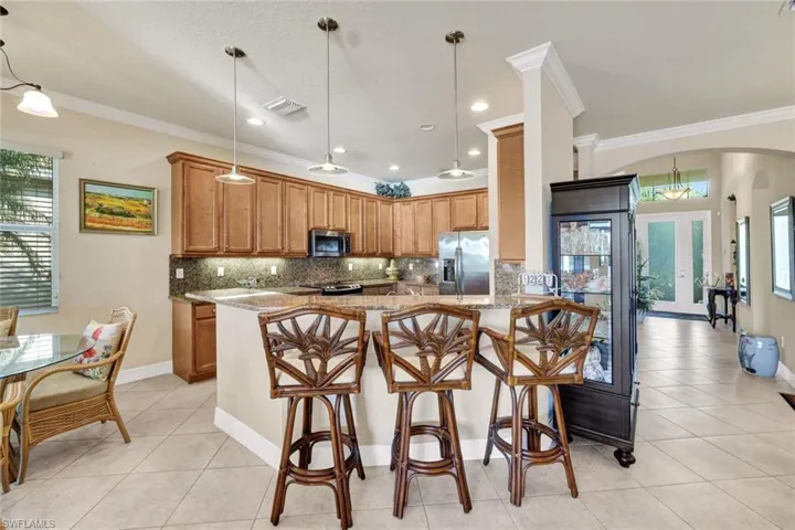 Kitchen featuring crown molding, hanging light fixtures, light stone countertops, kitchen peninsula, and stainless steel appliances