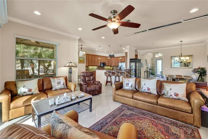 Living room featuring a wealth of natural light, light tile patterned flooring, ceiling fan with notable chandelier, and ornamental molding