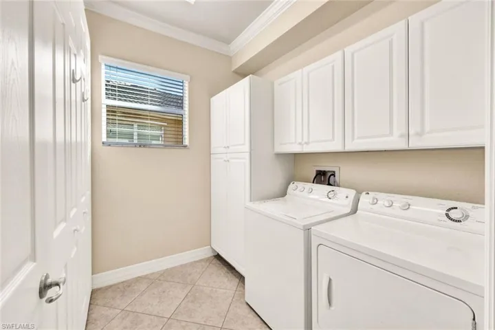 Washroom with washer and dryer, light tile patterned flooring, cabinets, and ornamental molding