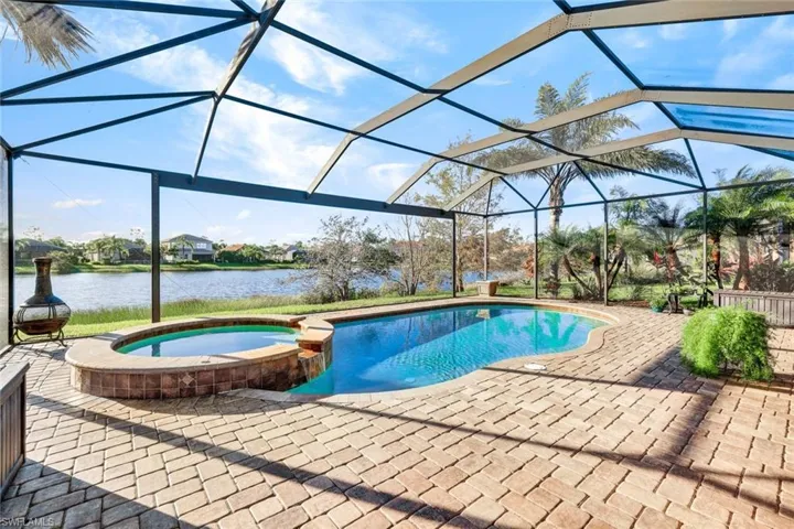 View of pool with an in ground hot tub, a water view, glass enclosure, and a patio area