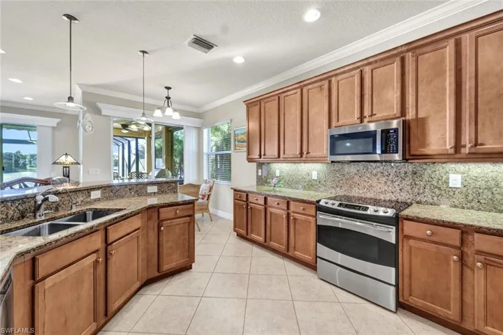 Kitchen featuring light stone countertops, appliances with stainless steel finishes, crown molding, sink, and decorative light fixtures