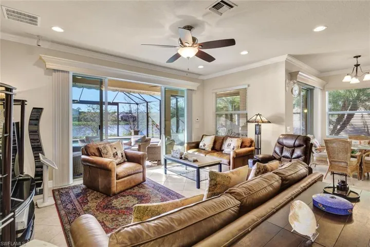 Living room with ceiling fan with notable chandelier, crown molding, and light tile patterned flooring