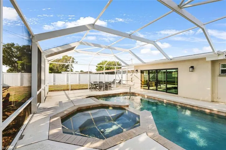 View of swimming pool featuring a patio area, glass enclosure, and an in ground hot tub