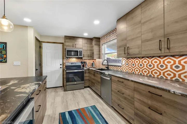 Kitchen with light hardwood / wood-style floors, hanging light fixtures, stainless steel appliances, backsplash, and sink