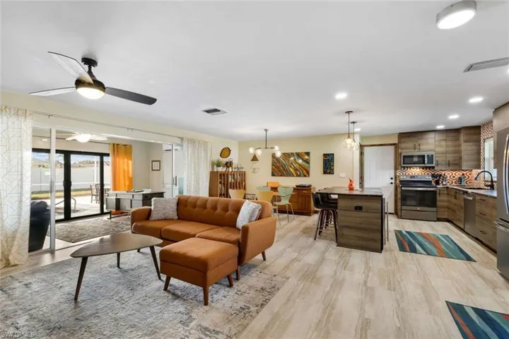 Living room featuring ceiling fan with notable chandelier, light wood-type flooring, and sink