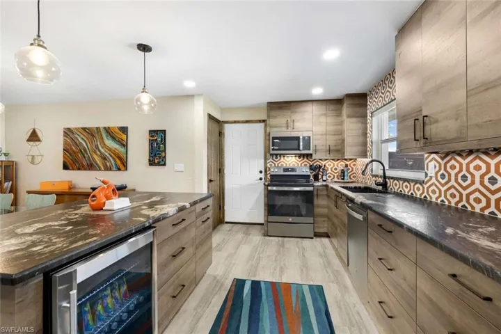 Kitchen featuring light hardwood / wood-style floors, beverage cooler, backsplash, hanging light fixtures, and appliances with stainless steel finishes