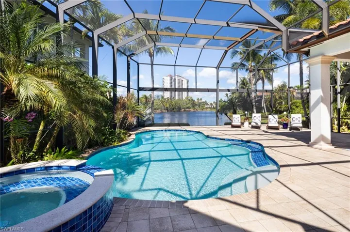 View of swimming pool featuring a pool with connected hot tub, a patio area, glass enclosure, and a water view