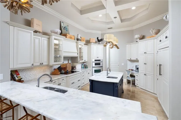 Kitchen with glass insert cabinets, tasteful backsplash, coffered ceiling, hanging light fixtures, and beamed ceiling