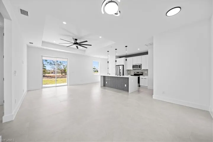 Unfurnished living room with a ceiling fan, a tray ceiling, and recessed lighting