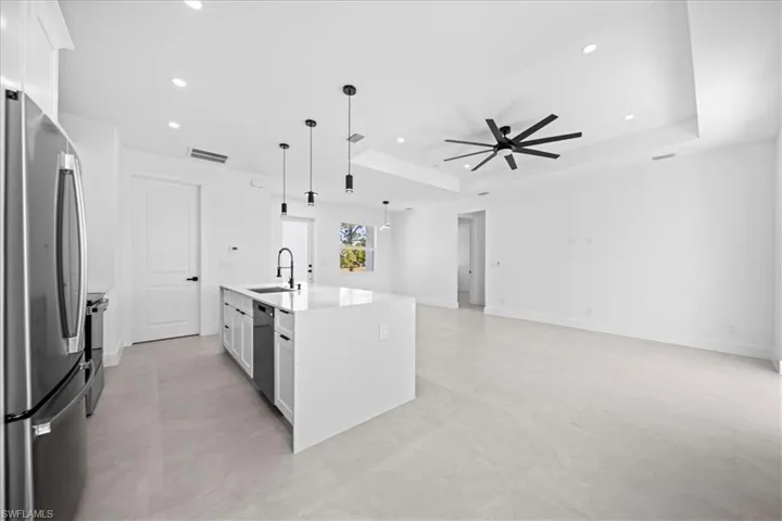 Kitchen featuring stainless steel appliances, decorative light fixtures, a kitchen island with sink, light stone counters, and a tray ceiling