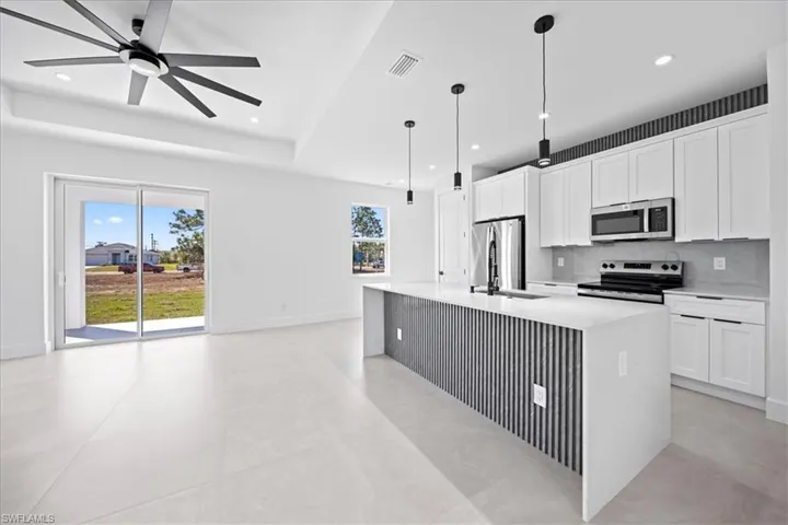 Kitchen featuring white cabinetry, stainless steel appliances, a ceiling fan, and light stone counters