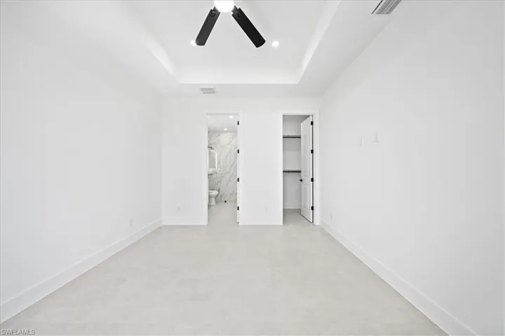 Unfurnished bedroom with a spacious closet, a tray ceiling, ceiling fan, and recessed lighting