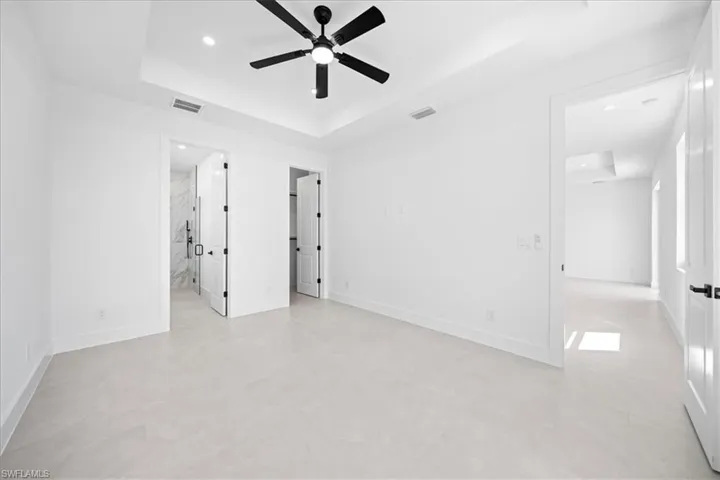 Unfurnished bedroom with a tray ceiling, recessed lighting, ceiling fan, and connected bathroom