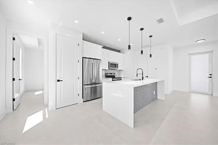 Kitchen featuring stainless steel appliances, white cabinets, a kitchen island with sink, light stone countertops, and decorative light fixtures